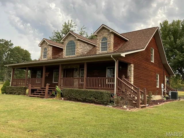 View of front facade featuring covered porch, stone siding, and a front yard