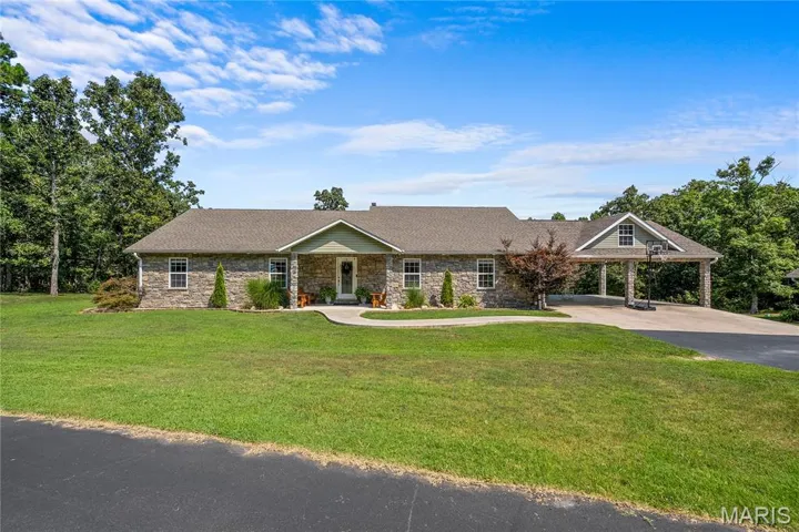 Single story home featuring stone siding, asphalt driveway, a front lawn, roof with shingles, and a carport