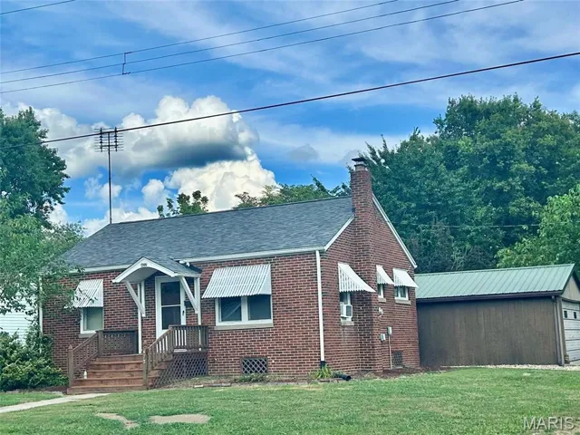 View of front of property with a chimney, a front yard, brick siding, and roof with shingles