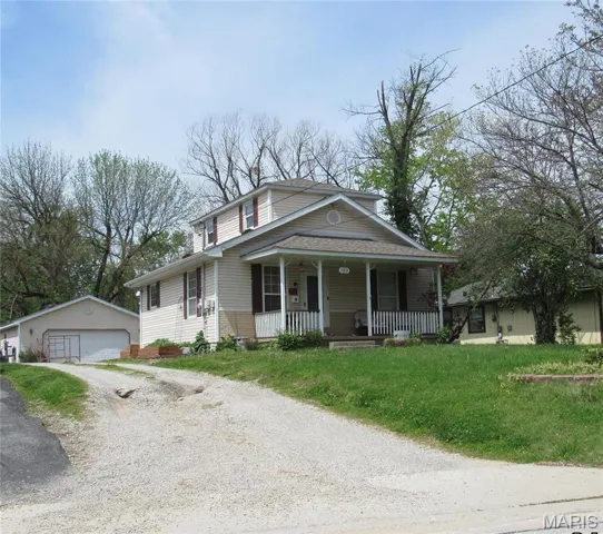 View of front of house featuring an outdoor structure, covered porch, a shingled roof, a detached garage, and a front lawn