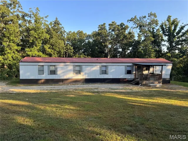 Manufactured / mobile home featuring a front yard, a metal roof, and view of wooded area