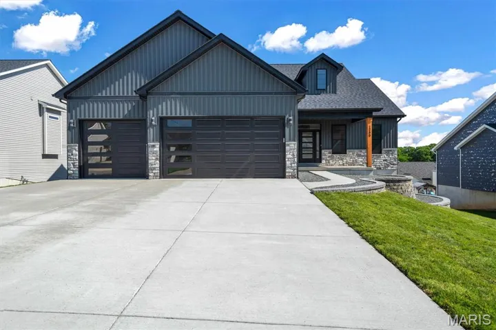 View of front of property featuring board and batten siding, stone siding, an attached garage, a front yard, and concrete driveway