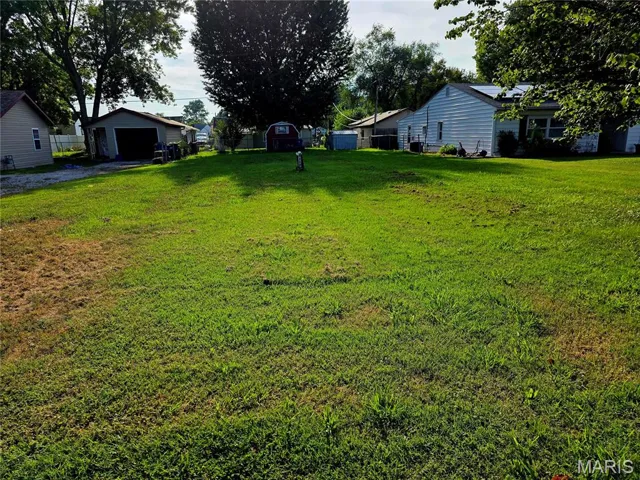 View of green lawn featuring an outdoor structure, a garage, and a residential view