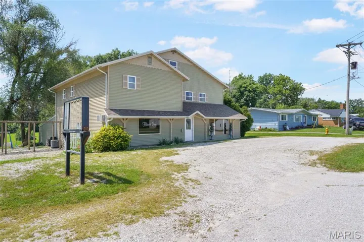 View of front of property featuring gravel driveway, covered porch, and a front lawn