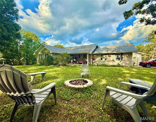 Back of house featuring a fire pit, a shingled roof, brick siding, a yard, and a patio area