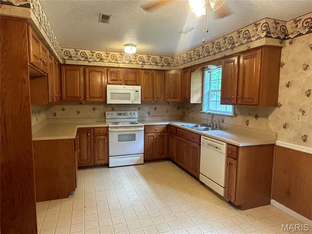 Kitchen featuring wallpapered walls, brown cabinets, white appliances, light countertops, and a textured ceiling