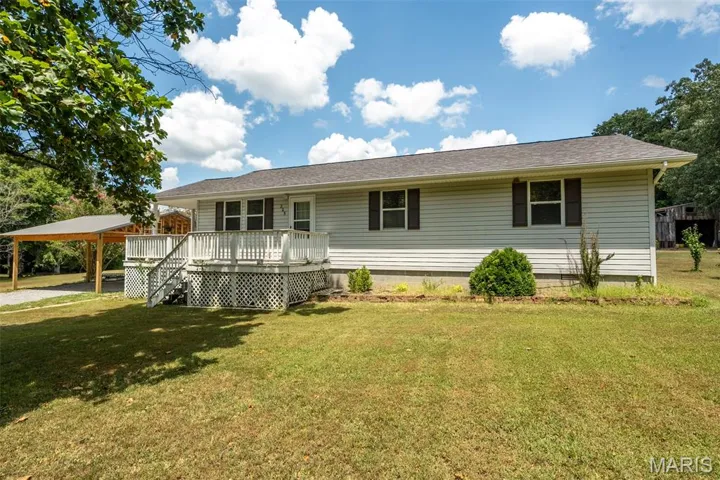 Ranch-style house featuring a front lawn, a wooden deck, and roof with shingles