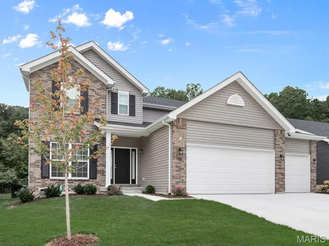 View of front of house with an attached garage, a front lawn, brick siding, and driveway