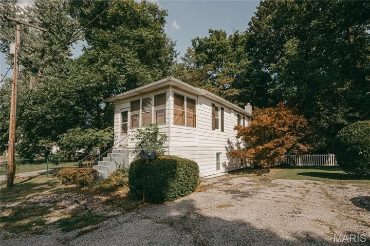 View of home's exterior with a sunroom and view of wooded area