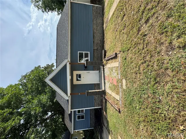 View of front of property featuring stone siding, a front yard, and roof with shingles