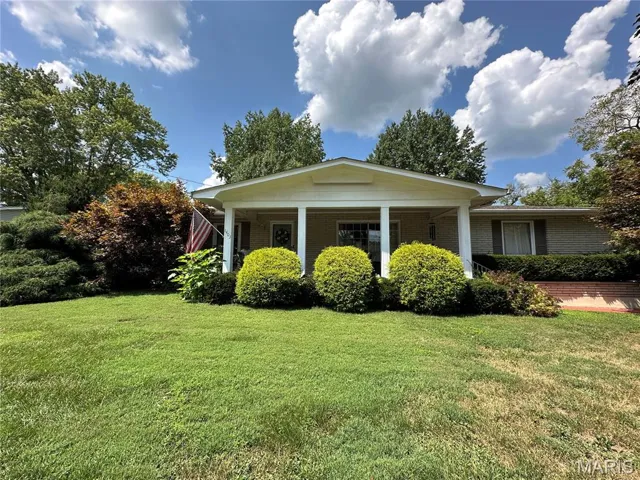 View of side of home with a lawn, brick siding, and a porch