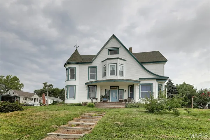 Victorian-style house with a porch, a front lawn, a chimney, and a shingled roof