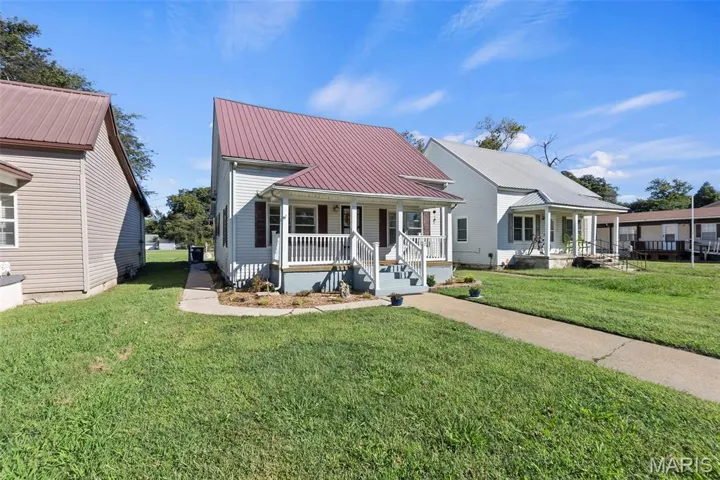 View of front of house with a porch, a front lawn, and a metal roof