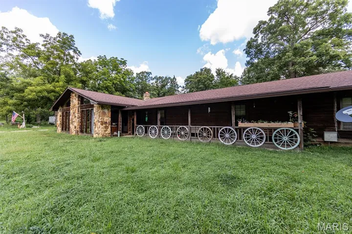 Back of property with stone siding, a lawn, a chimney, and a shingled roof