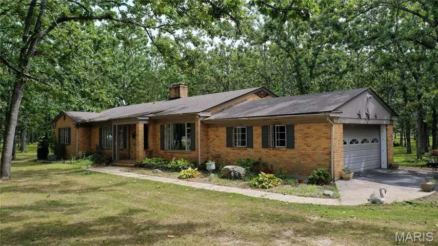 Ranch-style home with brick siding, an attached garage, a chimney, a shingled roof, and a front yard