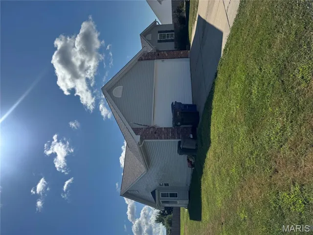 View of side of property with brick siding, driveway, a lawn, a garage, and a shingled roof
