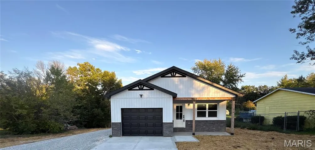Modern inspired farmhouse with stone siding, covered porch, concrete driveway, and a garage