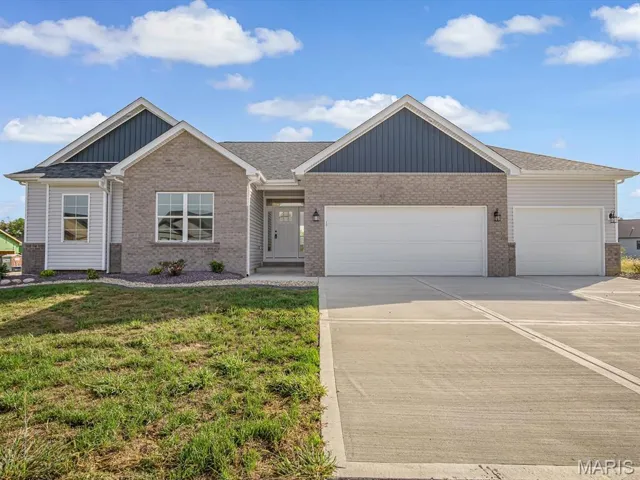 View of front of house featuring board and batten siding, concrete driveway, an attached garage, a front lawn, and brick siding