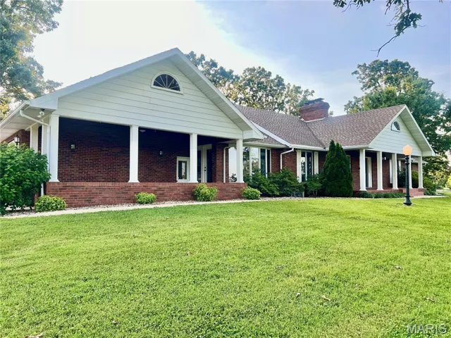 Ranch-style house with brick siding, covered porch, a front yard, and a chimney