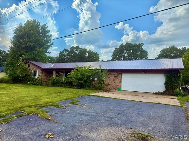 Ranch-style home with brick siding, a metal roof, asphalt driveway, a front lawn, and a garage
