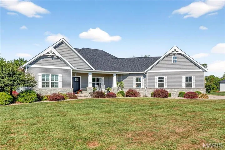 Craftsman-style house featuring stone siding, a porch, a front yard, and a shingled roof