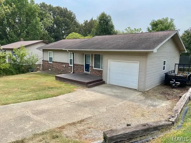 Ranch-style house featuring concrete driveway, a front lawn, brick siding, a deck, and a garage