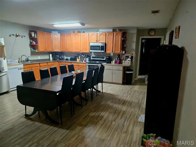 Kitchen featuring open shelves, appliances with stainless steel finishes, light wood finished floors, and light countertops