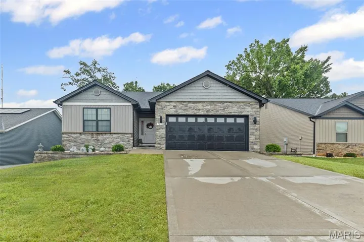 View of front facade with stone siding, an attached garage, concrete driveway, and a front lawn