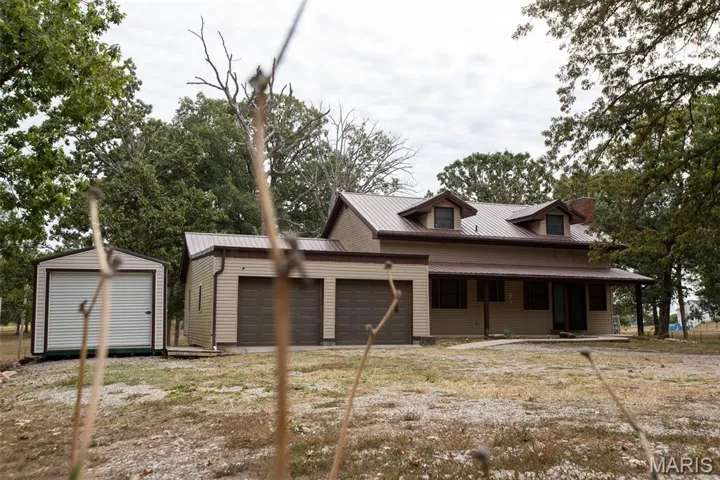 View of front of home featuring a porch, an attached garage, a metal roof, and a shed