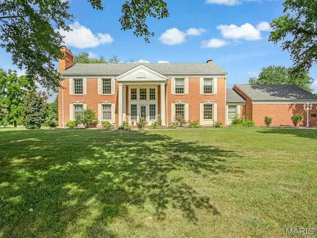 Greek revival inspired property with a chimney, a front yard, and brick siding