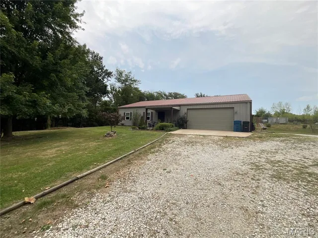 Ranch-style home featuring a metal roof, an attached garage, driveway, and a front lawn