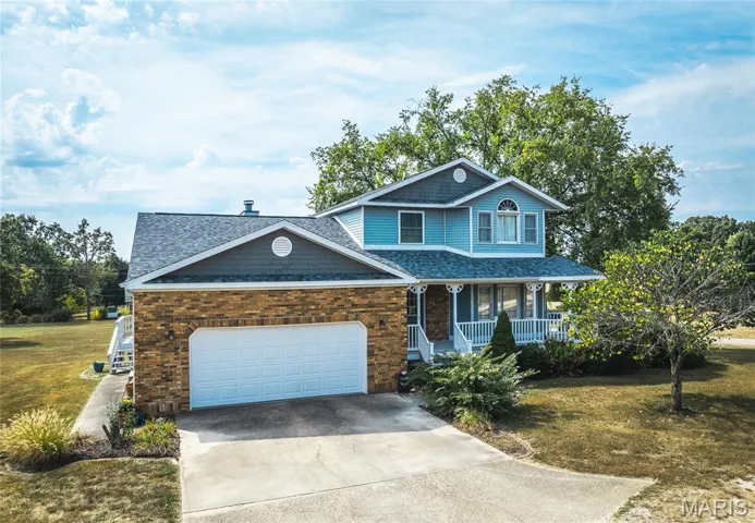 View of front facade featuring covered porch, a shingled roof, concrete driveway, a front yard, and a garage