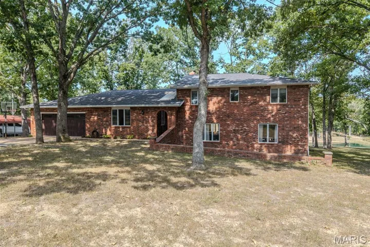 Back of house with brick siding, an attached garage, and a lawn