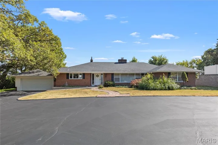Ranch-style house with brick siding, a chimney, asphalt driveway, a front lawn, and an attached garage