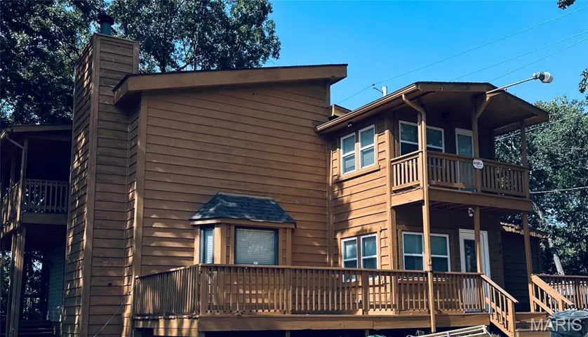 Rear view of property featuring a chimney, a balcony, and a deck