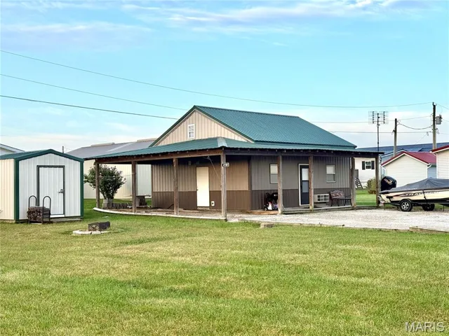 View of front of property with covered porch, a front yard, a storage shed, and a metal roof