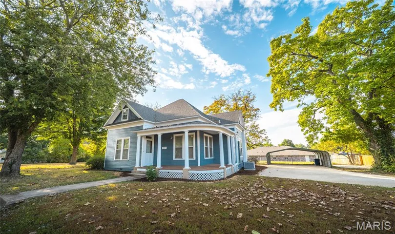 View of front of property with covered porch, a carport, driveway, and roof with shingles