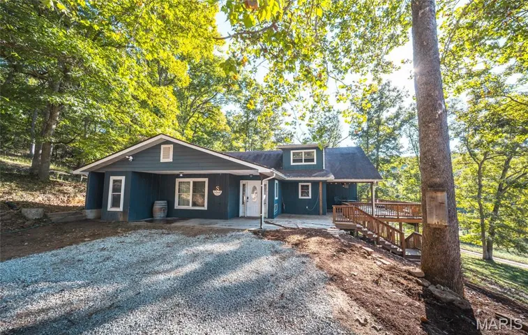 View of front of property with a patio, driveway, board and batten siding, and view of scattered trees