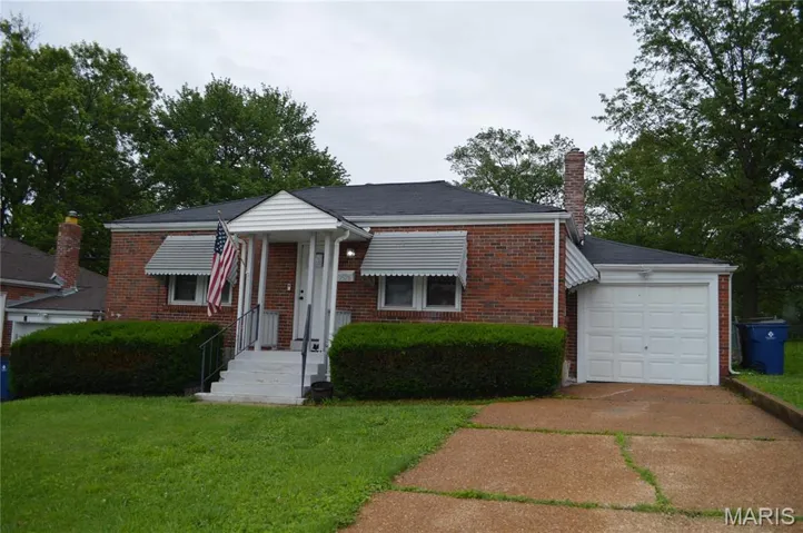 View of front facade featuring brick siding, a front lawn, a chimney, and driveway