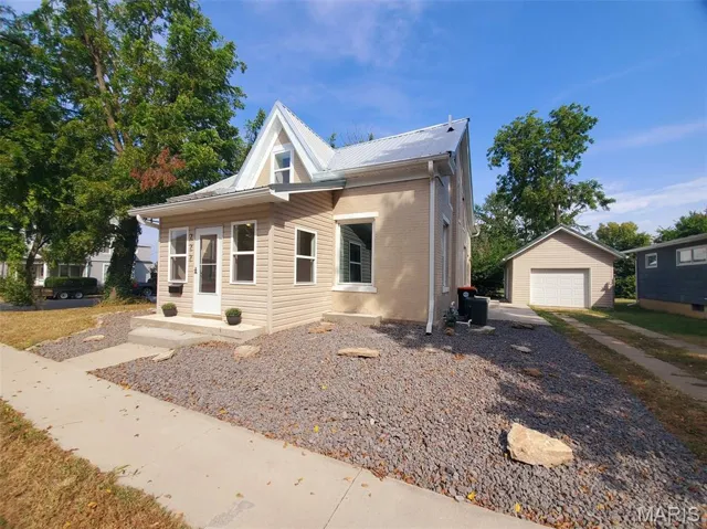 Bungalow with brick siding, an outdoor structure, a garage, a metal roof, and driveway
