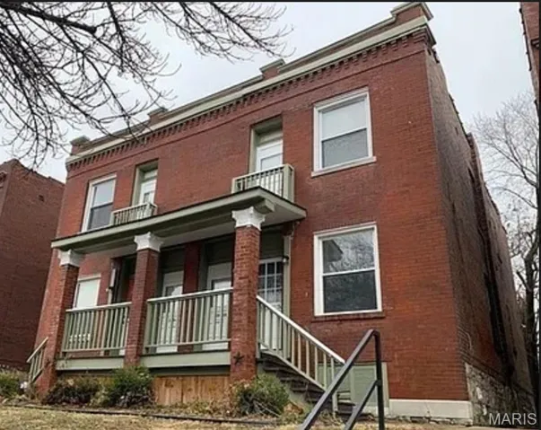 View of front of house featuring brick siding, covered porch, and a balcony