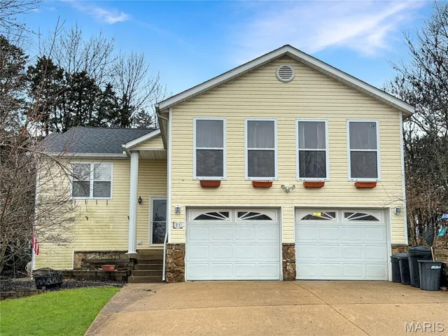 View of front of property with stone siding, an attached garage, driveway, and roof with shingles