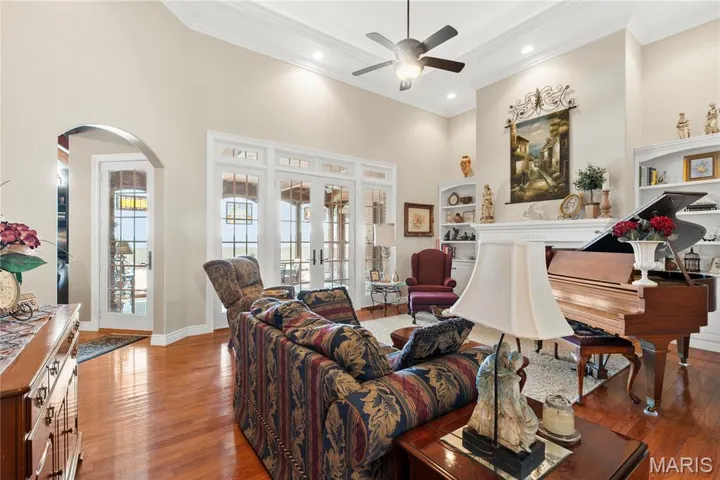 Living area with a towering ceiling, arched walkways, wood-type flooring, crown molding, and ceiling fan