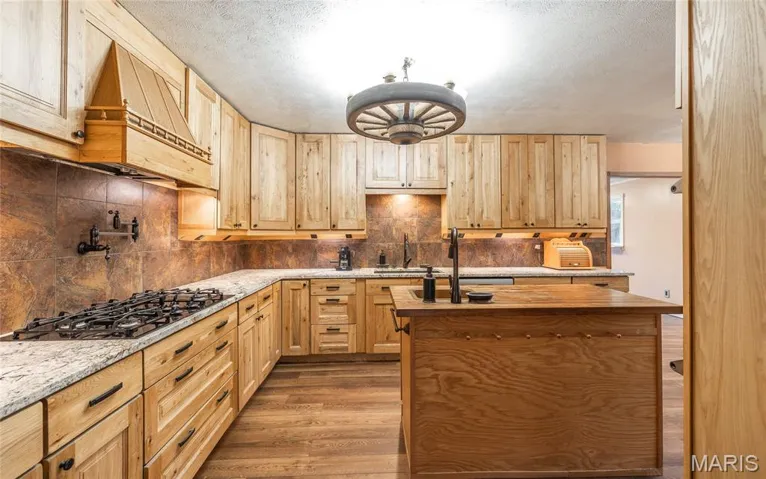 Kitchen with backsplash, light wood-type flooring, a kitchen island with sink, wooden counters, and a textured ceiling
