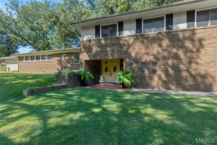 View of front of property featuring brick siding, a front yard, a balcony, and a patio