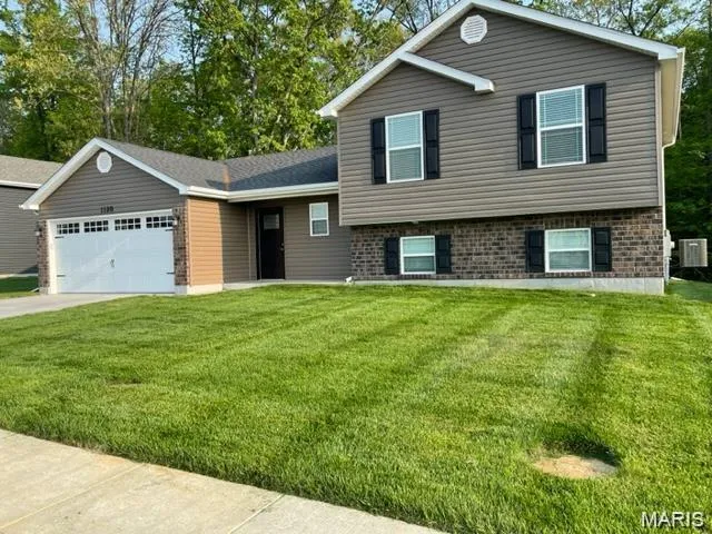 Split level home with a front yard, an attached garage, driveway, and brick siding