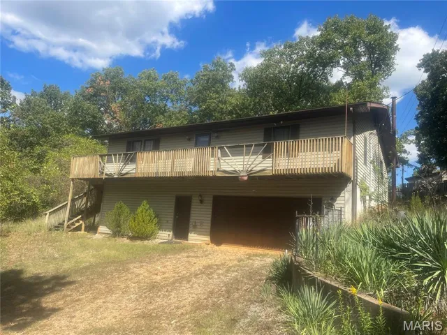 Rear view of house featuring dirt driveway, stairs, and a deck