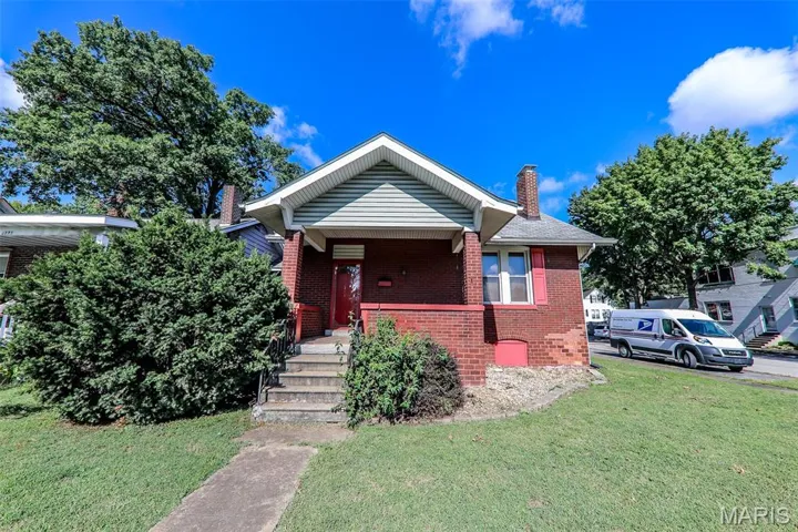 Bungalow featuring a chimney, brick siding, a front lawn, and covered porch