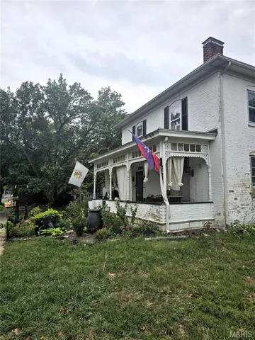 View of side of property featuring a chimney, brick siding, and a yard
