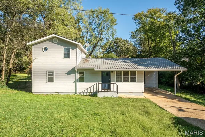 View of front of house with covered porch, a metal roof, driveway, an attached carport, and a front yard